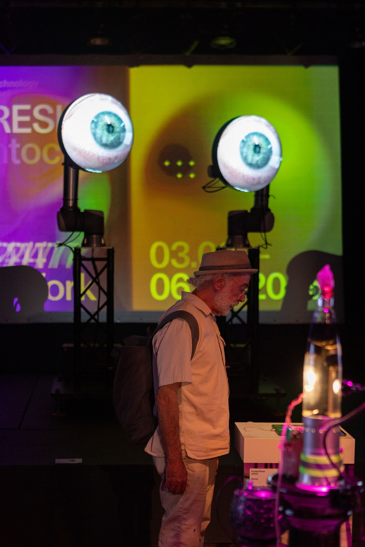 Im Vordergrund eine Person, die ein iPad anschaut. Im Hintergrund zwei grosse runde Screens in der Höhe mit je der Projektion eines offenen Auges darauf.