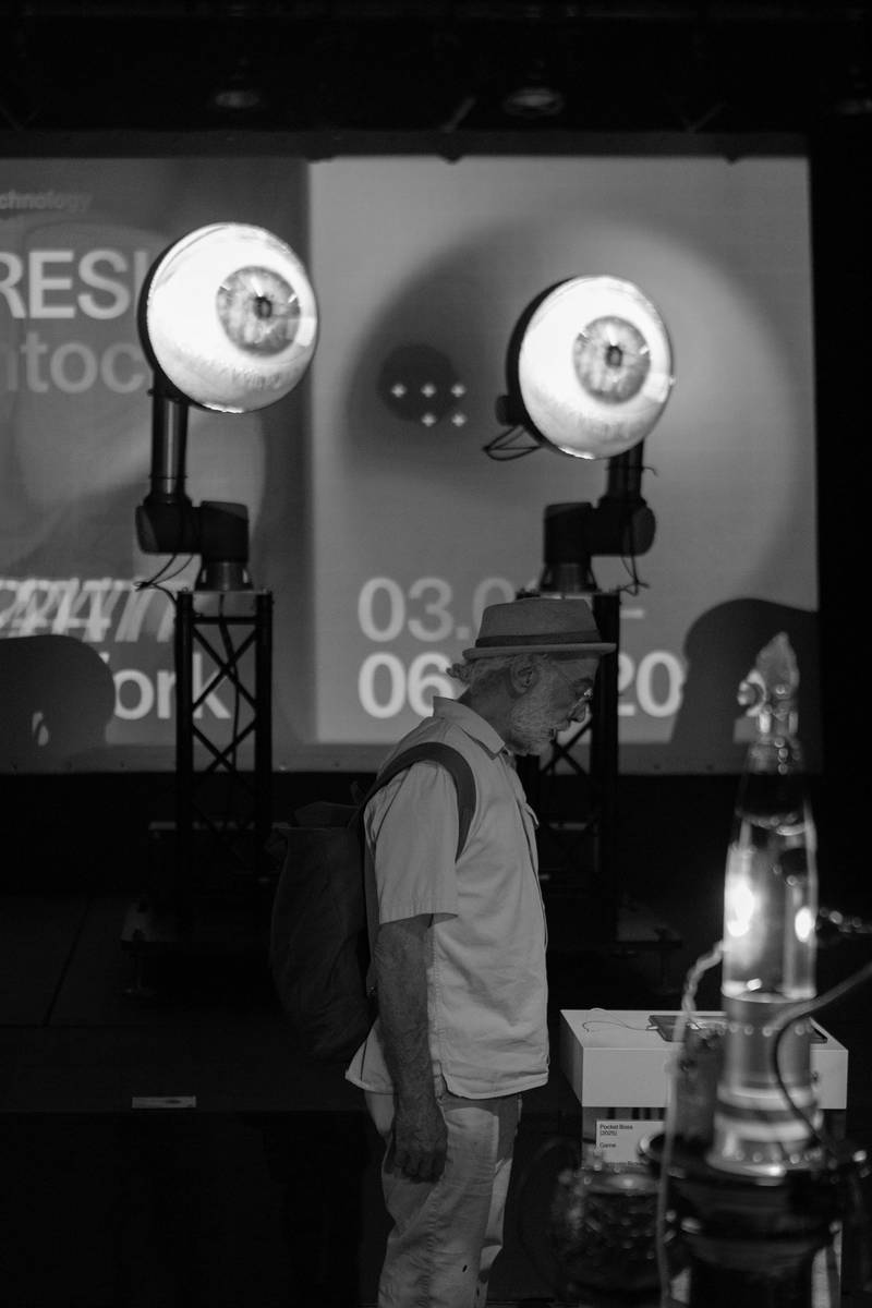 Im Vordergrund eine Person, die ein iPad anschaut. Im Hintergrund zwei grosse runde Screens in der Höhe mit je der Projektion eines offenen Auges darauf.