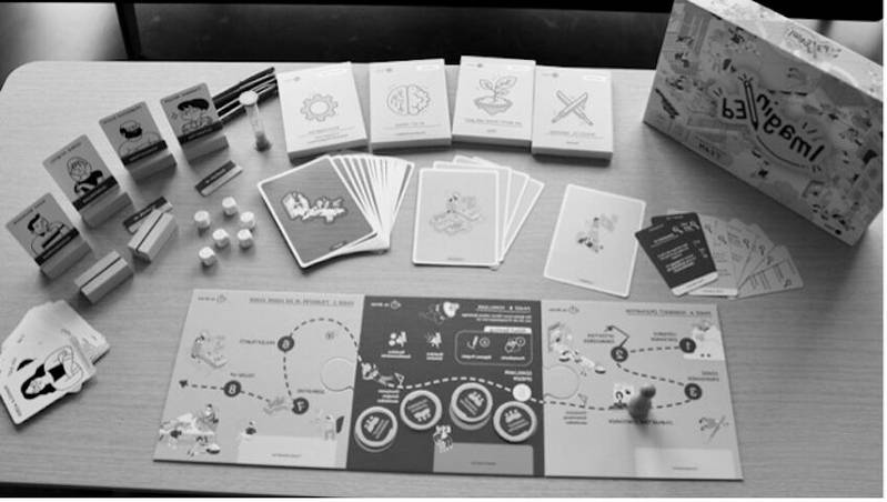 Der Inhalt des Spiel ist auf einem Tisch ausgebreitet. Neben einer Unterlage hat es verschiedenste Kärtchen, Chips und Würfel.