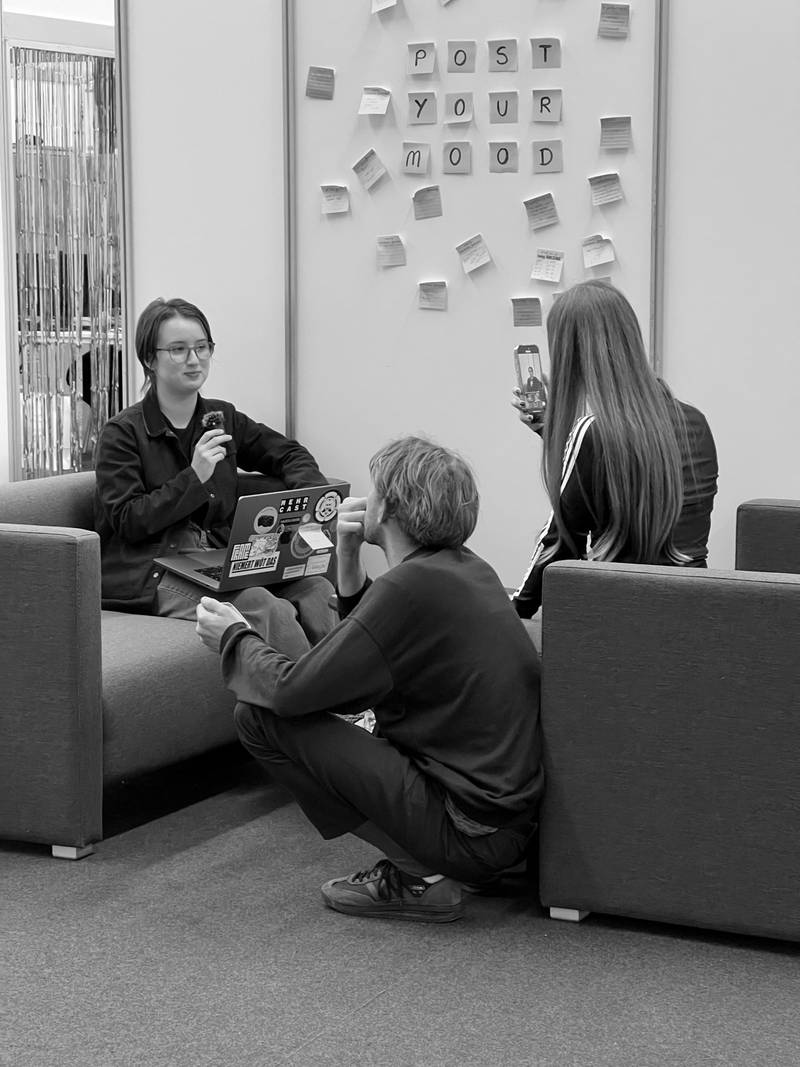 Cast students are sitting on sofas and record a video using a microphone and a phone camera. Post-its on the wall say: "Post Your Mood". Credits: Nadia Holdener.