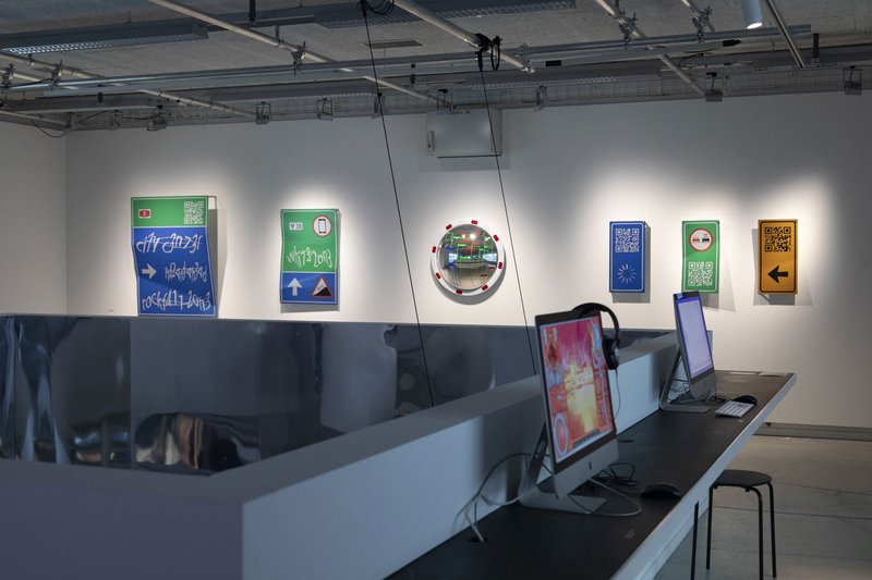 Ausstellung in der Galerie 2. An der Wand sind Exponate (Verkehrsschilder mit ungewöhnlicher Schrift) angebracht. © David Jäggi.