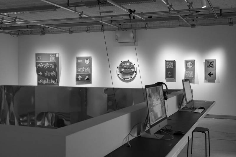 Ausstellung in der Galerie 2. An der Wand sind Exponate (Verkehrsschilder mit ungewöhnlicher Schrift) angebracht. © David Jäggi.