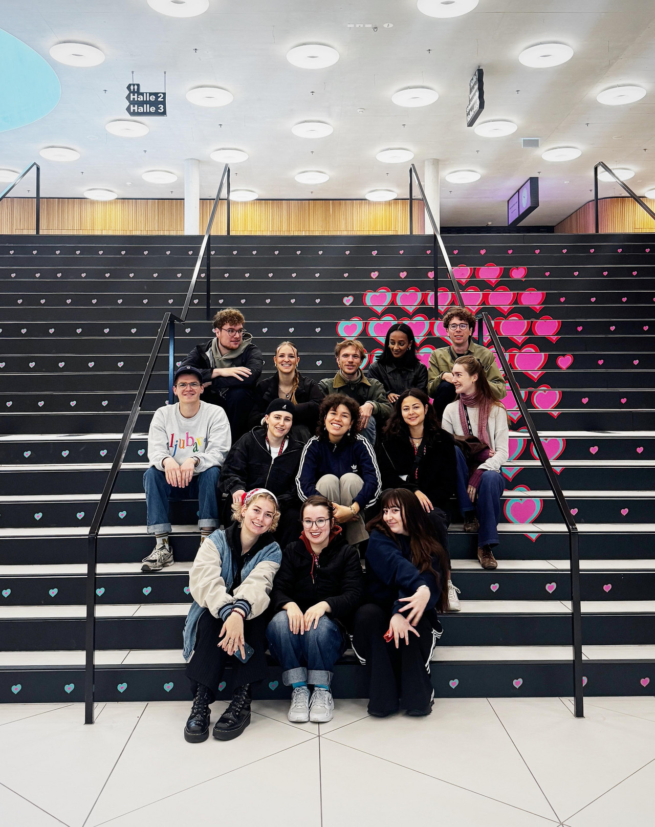 Cast students sitting on stairs with the ESC logo (many little hearts) dem ESC-Logo. Credits: Nadia Holdener.