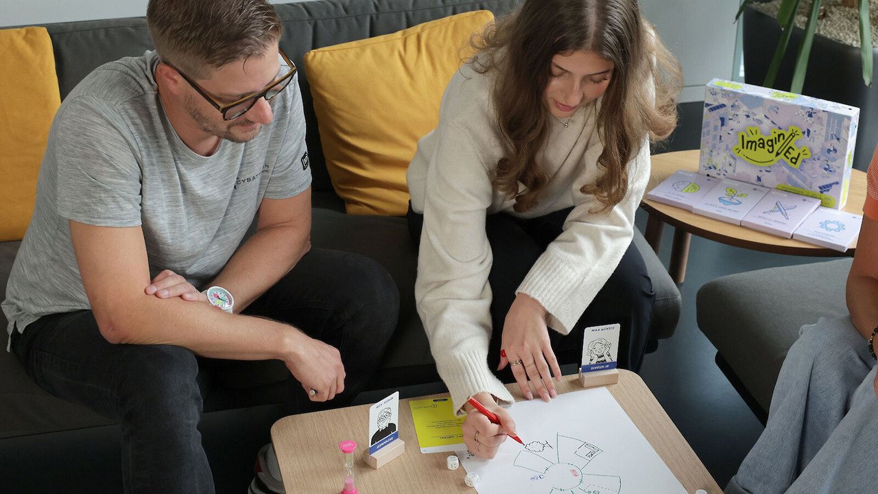 Zwei Personen sitzen vor dem Spiel und erstellen ein handschriftliches Mindmap.