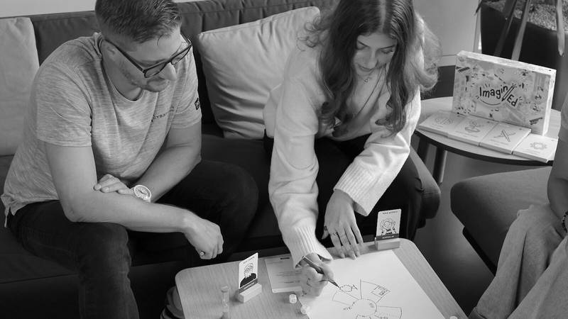 Zwei Personen sitzen vor dem Spiel und erstellen ein handschriftliches Mindmap.