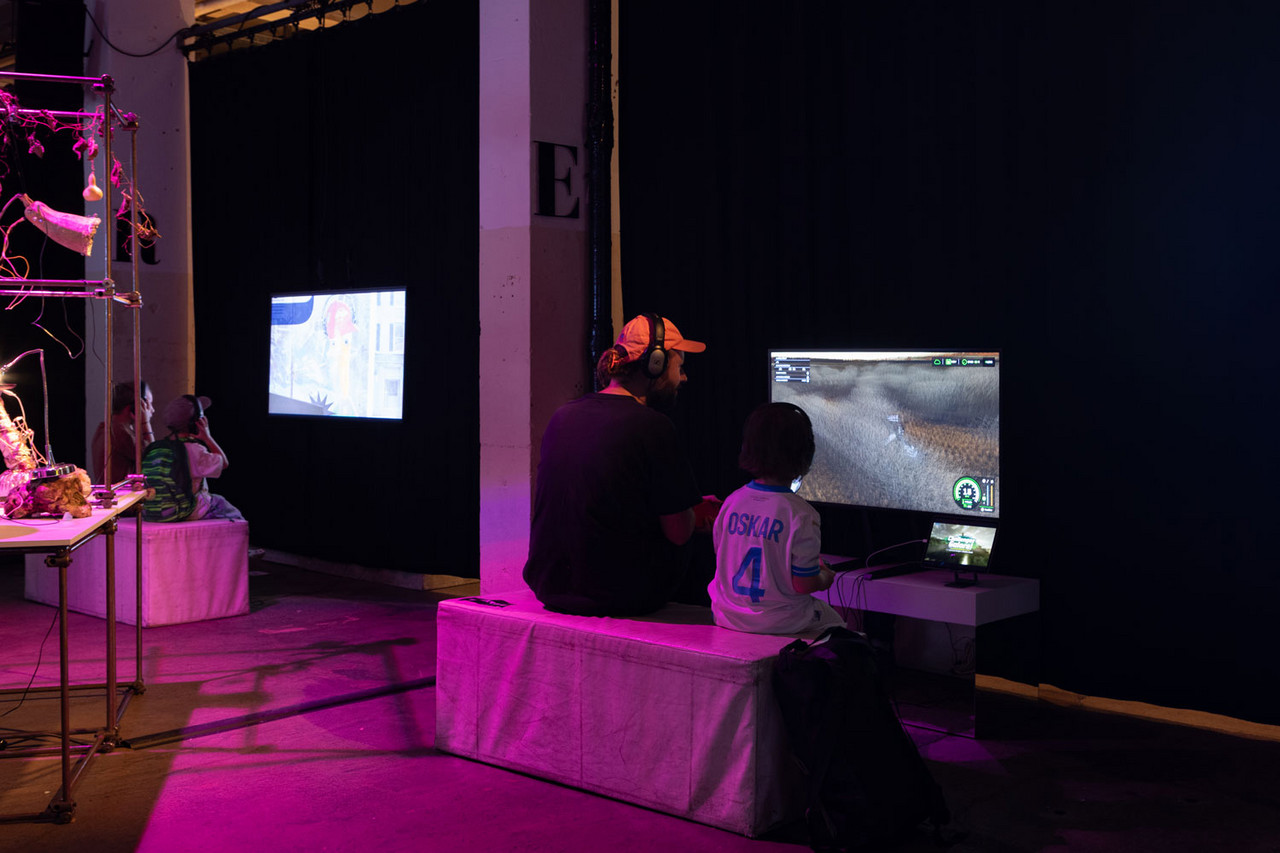 Besuchende vor zwei Screens - einem Film und einem Videospiel.