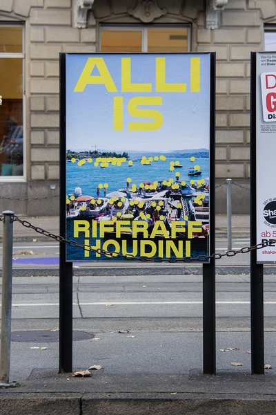 Plakat der Kampagne «Alli is Riffraff/Houdini» auf einer Verkehrsinsel. Auf dem Plakat sind viele Menschen am See zu sehen, alle Gesichter sind kleine gelbe Punkte. Gelbe Schrift: «Alli is Riffraff/Houdini».